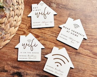 May include: Four white wooden house-shaped signs with wifi symbols and text. The signs say "But first wifi", "Make yourself at home", "Wifi is on the house", and "Wifi". The signs have a network and password field.