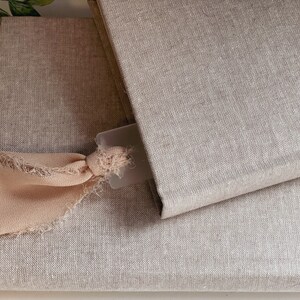 May include: Two linen-covered journals with a light pink ribbon bookmark. The top journal is closed and the bottom journal is open.