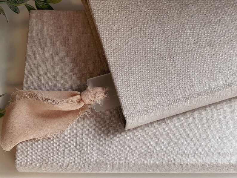 May include: Two linen-covered journals with a light pink ribbon bookmark. The top journal is closed and the bottom journal is open.