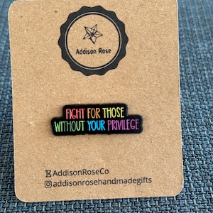 Puede incluir: Pin con el texto "FIGHT FOR THOSE WITHOUT YOUR PRIVILEGE" en colores del arcoíris sobre fondo negro. El pin está sobre una tarjeta marrón con el logotipo "Addison Rose" y su nombre de usuario en redes sociales.