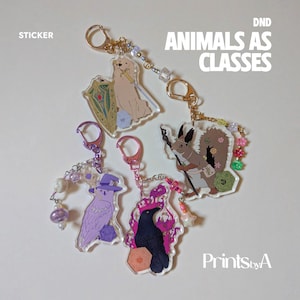 Pode incluir: Quatro porta-chaves em acrílico com ilustrações de animais DND como classes: um cão dourado com escudo, um esquilo com cajado, uma coruja roxa com chapéu de feiticeiro e um corvo preto com chamas cor-de-rosa, com fecho metálico e missangas.