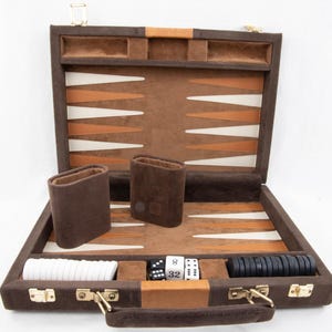 May include: Open backgammon set in a brown case with a tan and white playing surface. The set includes brown dice cups, white and black game pieces, and dice. The case is open, revealing the game pieces and playing board.