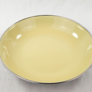 May include: A yellow enamelware baking dish with black handles. The dish is round and has a smooth, glossy finish.