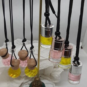 May include: A set of car air fresheners with different scents and colours. The fresheners are hanging from black cords with wooden beads. The fresheners are displayed on a gold metal stand with a marble base. A small gold statue of Buddha is sitting on the marble base.