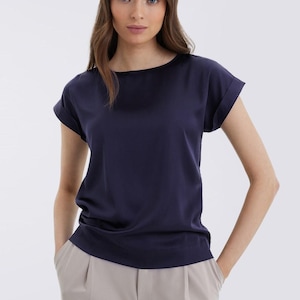 Könnte beinhalten: Ein marineblaues T-Shirt mit kurzen Ärmeln, lockerer Passform und hochgekrempelten Ärmeln.