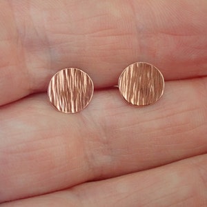 May include: A pair of small, round, rose gold earrings with a textured surface.