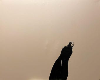 May include: A black silhouette of a person wearing a head covering and a long coat, standing against a light beige background.