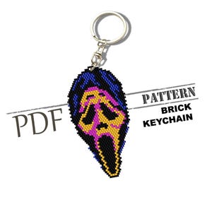 May include: A black, blue, yellow, and pink brick keychain featuring a Scream mask design. The keychain has a silver ring and clasp. The words "PATTERN BRICK KEYCHAIN" are printed on the image.