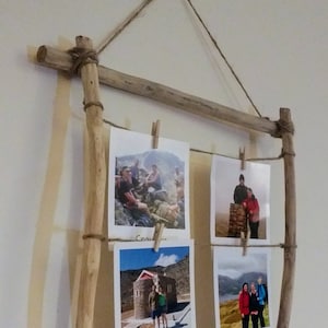 May include: A rustic wooden picture frame with twine hanging from the top. The frame holds four photos with handwritten captions: "Crete", "Buttermere", and two others.