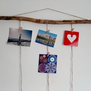 May include: A rustic wooden branch with twine strung across it, holding five photos with clothespins. The photos include a landscape, a building, a heart, and two abstract designs.
