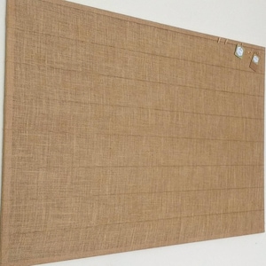 May include: A large, brown burlap bulletin board with a grid pattern. There are three small, white paper tags hanging from the top with string.