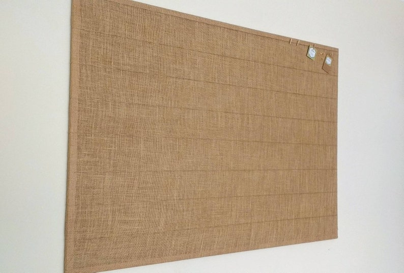 large cork board covered in natural hessian with jute strings across for hanging photos and notes with mini pegs.