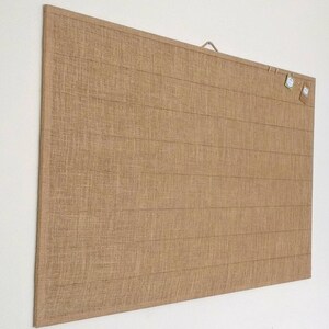 May include: A large, rectangular burlap bulletin board with a wooden frame and a metal hanging hook. The board has a natural brown color and a textured surface.