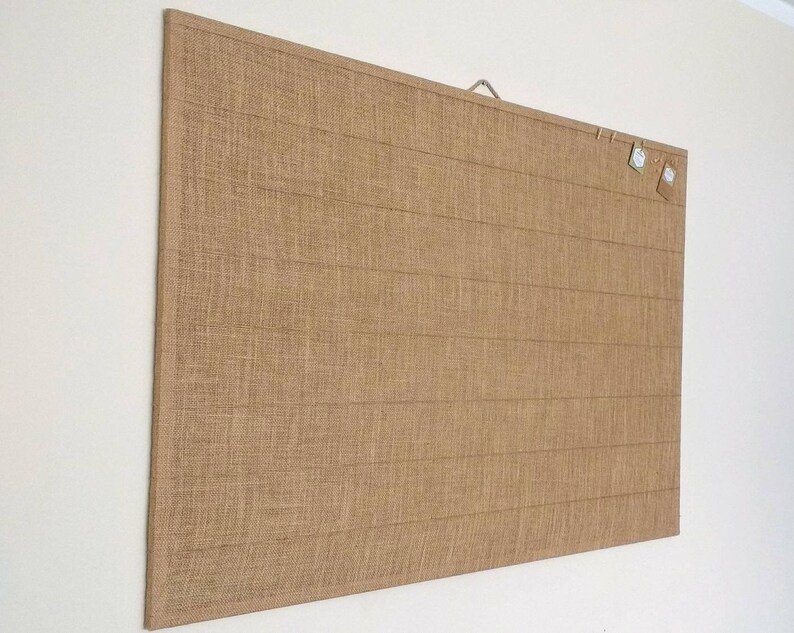 May include: A large, rectangular burlap bulletin board with a wooden frame and a metal hanging hook. The board has a natural brown color and a textured surface.