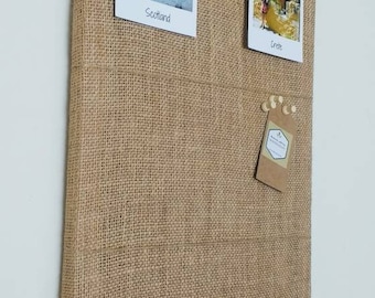 May include: A brown burlap cork board with two photos pinned to it. The photos are of a castle in Scotland and a building in Crete. The cork board has a small brown tag pinned to it with the text "Handmade with Love by WOODENLY".