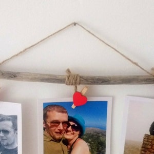 May include: A rustic driftwood photo display with three photos hanging from twine. Each photo is held in place with a wooden clothespin with a red heart attached.