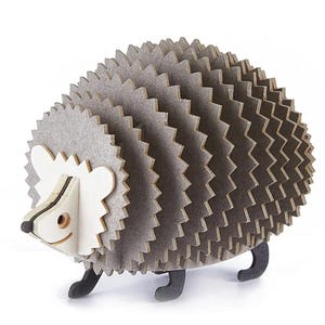 May include: A wooden hedgehog sculpture with a layered design. The body features numerous grey, zig-zag shaped layers, while the face and ears are white. The hedgehog has black legs and a small, smiling face. This decorative item is suitable for home decor.