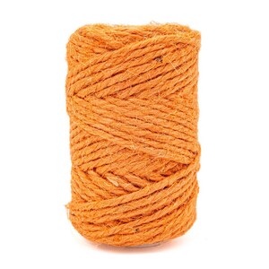 May include: A cylindrical spool of bright orange twine made from natural fibrous material. The cord is tightly wound in a continuous spiral pattern, showcasing a textured, rustic surface with visible loose fibres throughout the entire length.