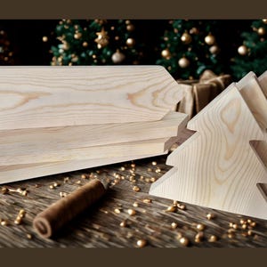 May include: A collection of unfinished wooden Christmas tree cutouts and rectangular wooden pieces. The light-colored wood has visible grain patterns. A small, rolled brown object and scattered gold-colored beads are also present.