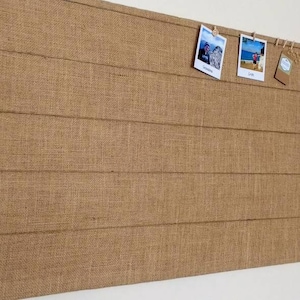 May include: A brown burlap bulletin board with a wood-like texture. The board has five horizontal lines and is decorated with three photos and a small tag.