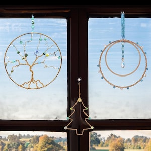 May include: Three decorative window ornaments. One is a tree of life design, another is a double-hoop with a crystal pendant, and the third is a Christmas tree shape. All are made of wire and adorned with beads.