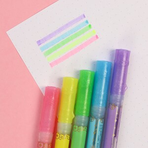May include: A set of six highlighter pens with a rainbow of colors, including purple, blue, green, yellow, and pink. The pens have a glittery finish and are arranged in a row.