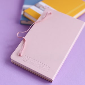 May include: A pink notebook with a light pink ribbon closure and the text "The Collection" embossed on the cover.