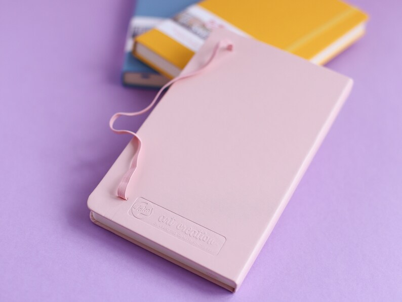 May include: A pink notebook with a light pink ribbon closure and the text "The Collection" embossed on the cover.