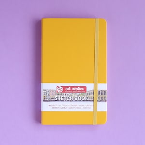 May include: A yellow sketchbook with a black and white illustration of a city on the front. The text on the front reads "art creation SKETCH BOOK 80 SHEETS/VEL/FEUILLES/BOGEN/HGIAS/LENZUOL 123/3 5400M/90BS-ACID FREE".