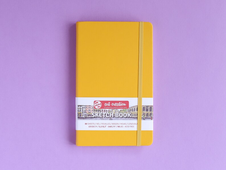 May include: A yellow sketchbook with a black and white illustration of a city on the front. The text on the front reads "art creation SKETCH BOOK 80 SHEETS/VEL/FEUILLES/BOGEN/HGIAS/LENZUOL 123/3 5400M/90BS-ACID FREE".