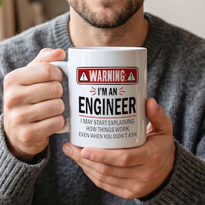 Peut inclure: Un mug en céramique blanche orné d'un panneau d'avertissement rouge et noir avec le texte WARNING: I'M AN ENGINEER I MAY START EXPLAINING HOW THINGS WORK EVEN WHEN YOU DIDN'T ASK. Le mug possède une anse standard et une finition lisse et brillante.