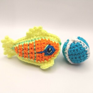 May include: A crocheted yellow fish with orange and green stripes and a blue eye, next to a crocheted blue and white ball.