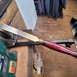 May include: A close-up of a Record Power RS8GG bench grinder with a sharpening jig attached. A chisel is being sharpened on the grinder.