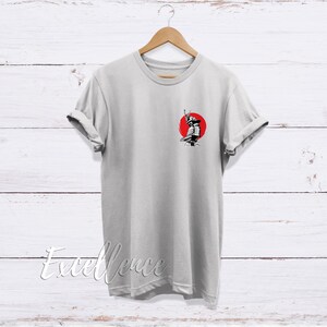 May include: A gray t-shirt with a black and white illustration of a samurai warrior standing in front of a red sun.