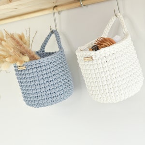 May include: Two hanging crocheted baskets, one in light blue and one in white. Both baskets have a wooden tag with the word "handmade" on them.