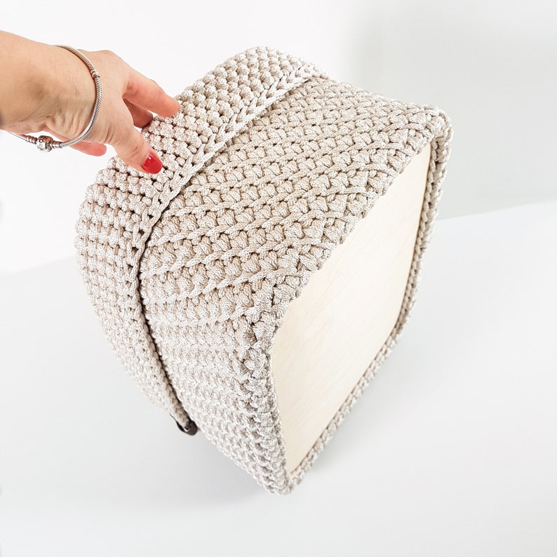 May include: A beige crocheted storage basket with a square shape and a textured pattern. The basket is made of a soft, yarn-like material.