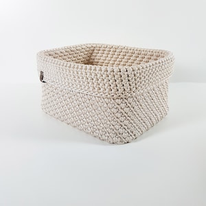 May include: A beige crocheted storage basket with a brown leather handle.