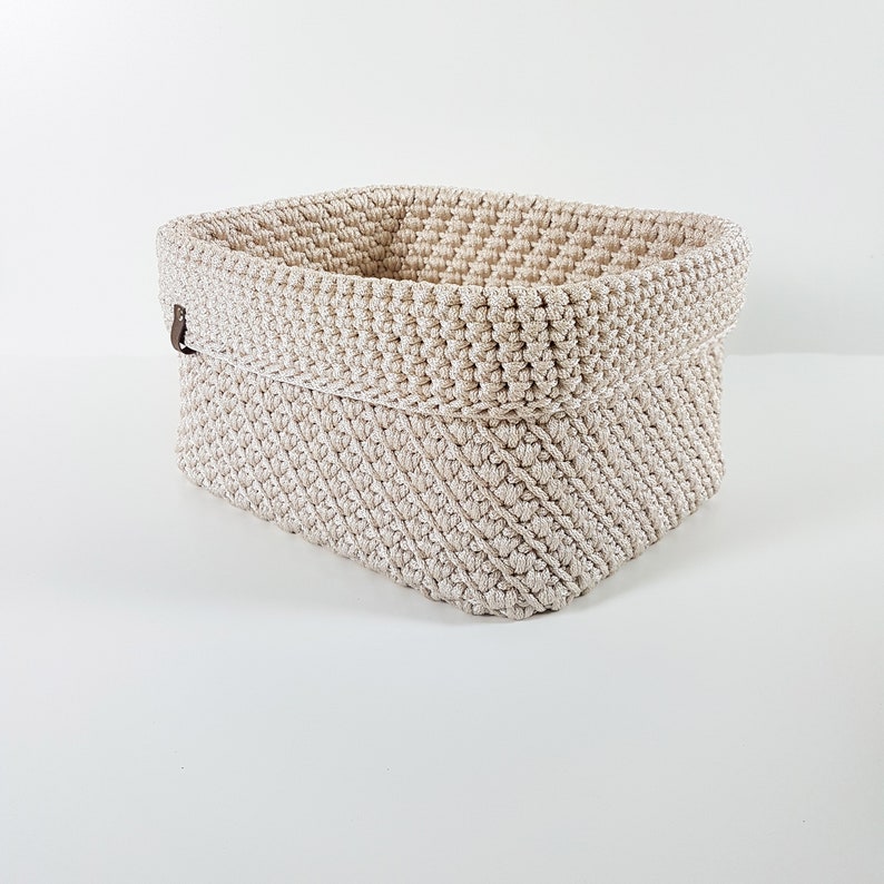 May include: A beige crocheted storage basket with a brown leather handle.