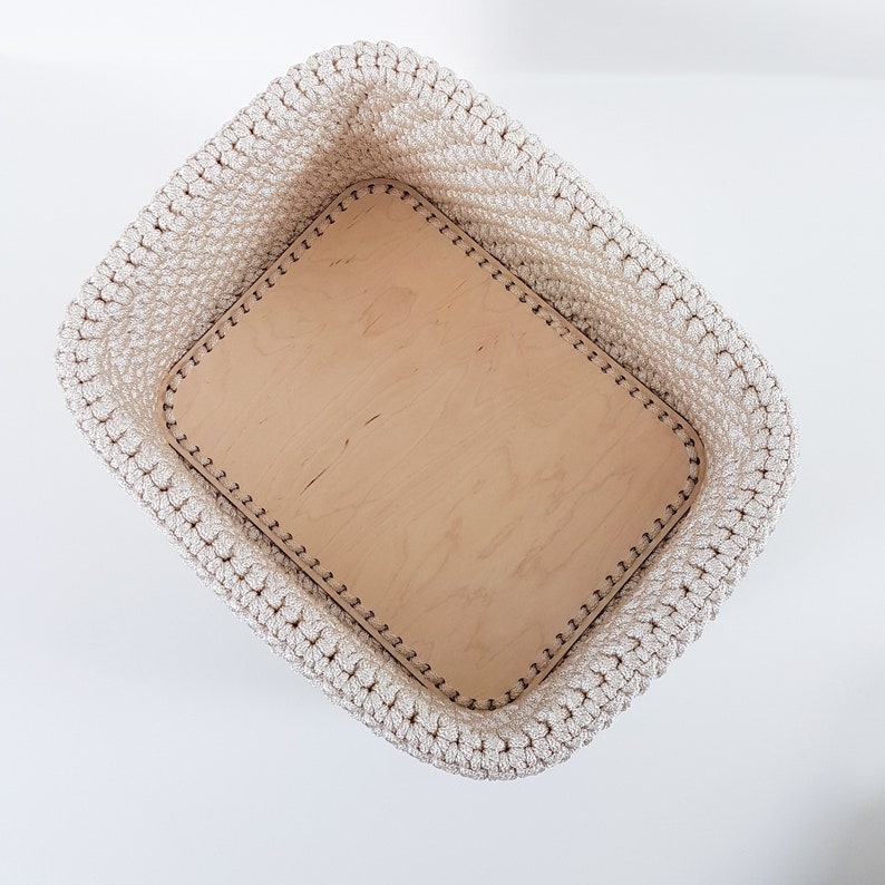 May include: A white crocheted storage basket with a beige leather insert. The basket is empty and has a decorative stitch around the edge.