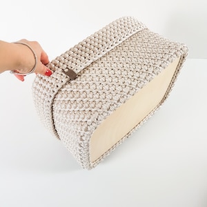 May include: A beige crocheted storage basket with a wooden base. The basket has a decorative brown leather strap.
