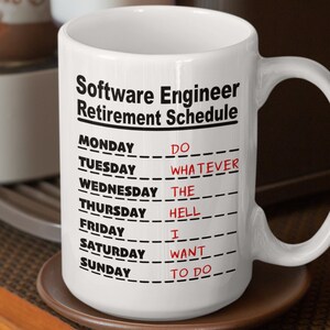 Könnte beinhalten: Eine weiße Keramik-Kaffeetasse mit einem schwarz-weißen Design, auf dem "Software Engineer Retirement Schedule" steht. Die Tasse hat einen schwarzen Henkel und steht auf einem braunen Untersetzer.