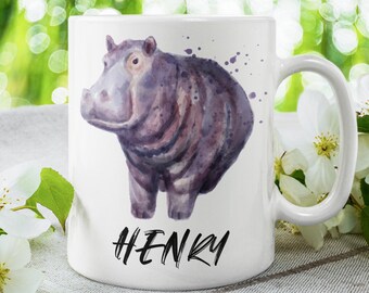 May include: White ceramic mug with a watercolor illustration of a purple hippopotamus. The mug has a black handle and the name "HENRY" is written in black at the bottom.