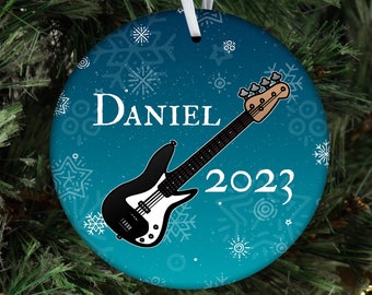 May include: A blue and white Christmas ornament with a black bass guitar and the name "Daniel" and the year "2023" on it.