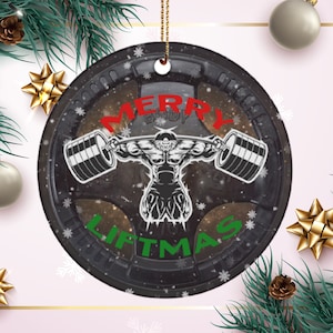 May include: A round Christmas ornament with a black and white image of a weightlifter lifting a barbell. The ornament has a white background with snowflakes and the text "Merry Liftmas" in green and red.