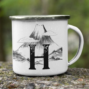 Peut inclure: Mug en émail blanc avec une illustration en noir et blanc d'une chaîne de montagnes et la lettre "H" sur le devant.