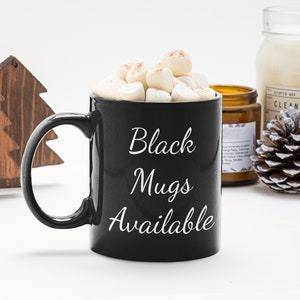 K&ouml;nnte beinhalten: Schwarze Keramiktasse mit wei&szlig;em Text, der "Black Mugs Available" lautet. Die Tasse ist mit hei&szlig;er Schokolade und Marshmallows gef&uuml;llt.