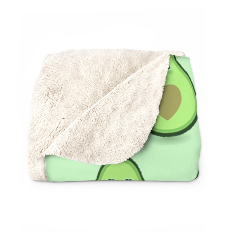 May include: A soft, plush throw blanket with a green background and a repeating pattern of avocado halves with a heart in the center. The blanket has a white sherpa lining.