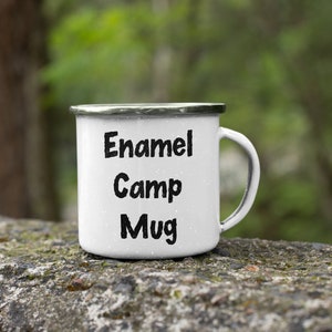 K&ouml;nnte beinhalten: Wei&szlig;e Emaille-Camping-Tasse mit schwarzem Text "Enamel Camp Mug".