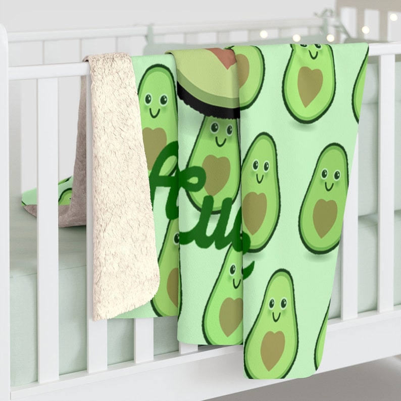 May include: A green and white fleece blanket with a pattern of smiling avocados with hearts. The text "Avo" is visible in the lower left corner of the blanket.
