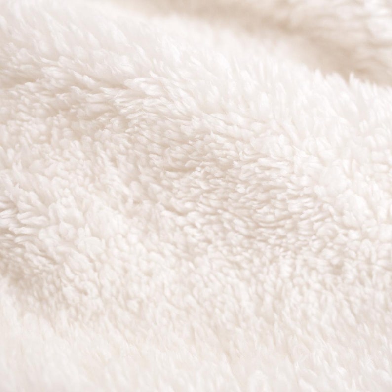 May include: Close-up of a soft, white, fluffy fabric with a textured surface.